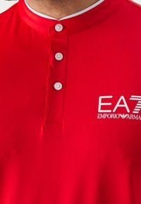 Chemise rouge avec col boutonné et logo blanc "EA7 Emporio Armani" sur la poitrine.