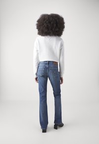 White cropped sweatshirt, blue denim jeans with a slight flare, and black block-heeled shoes. Smooth textures, minimalistic design, back view.