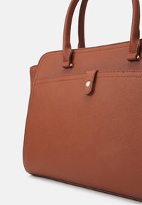 Sac à main synthétique marron avec surface texturée, doté de deux poignées, d'une fermeture par bouton-pression et de discrètes touches dorées.