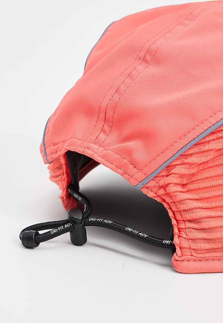 Casquette en tissu léger corail avec cordon noir ajustable et bord réfléchissant, conçue pour une utilisation athlétique ou en plein air.