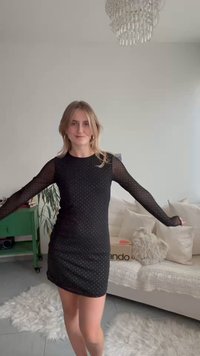 Musta mekko, jossa on pitkät, läpikuultavat hihat, vartalonmyötäinen siluetti, pilkkukuvio ja pyöreä pääntie vaaleaa taustaa vasten.