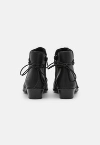 Bottes noires chevilles en cuir lisse, bout arrondi, petit talon et liens réglables à l'arrière. Doublure en polaire visible en haut.