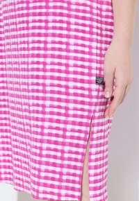 Vaaleanpunainen ja valkoinen ruudullinen mekko, jossa on sivuaukko ja tarra helmassa. Pehmeä kangas, jossa on sileä pinta. Takapuolet muotoa korostava malli.