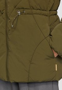 Groene pufferjack met rits, elastische trekkoord in de taille en zijzakken. Bevat een doorgestikte patroon en textuurstof.