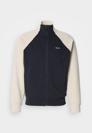 Sudadera con cremallera azul marino y crema con cuello alzado, mangas raglán, bolsillos delanteros y logo "BOSS" en el pecho. Textura de tela suave.