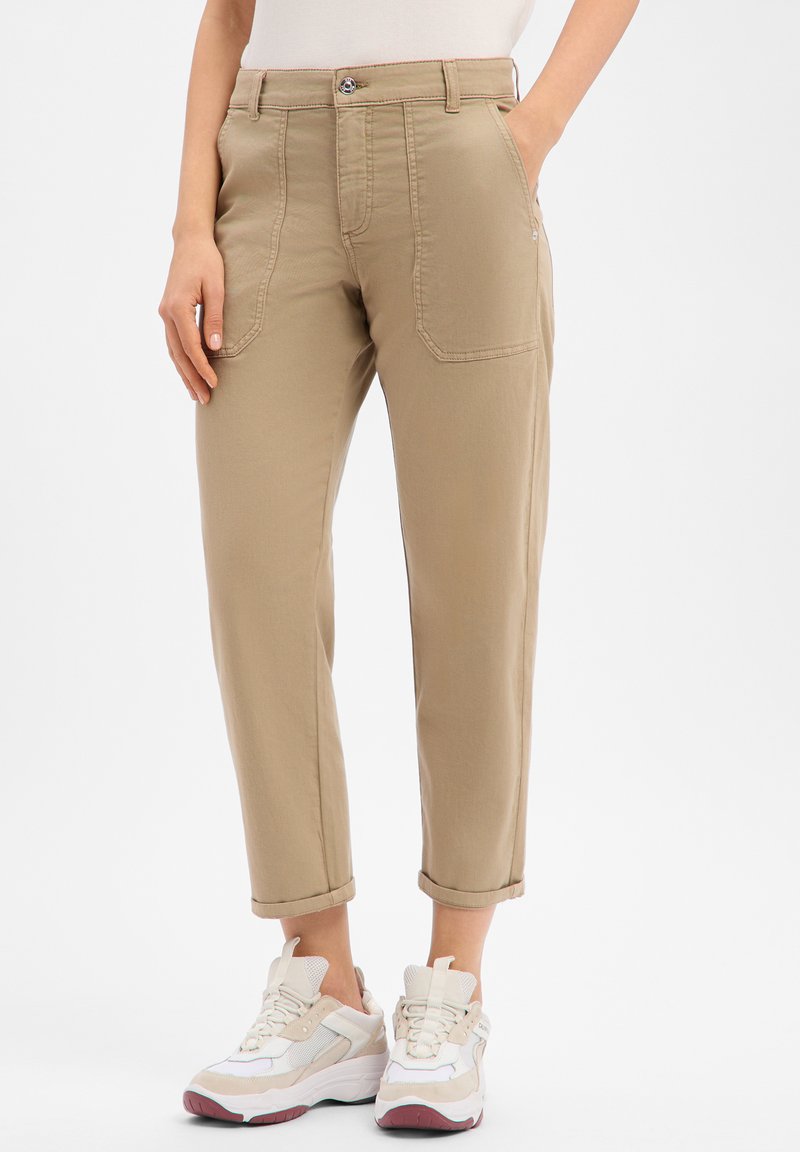 Pantalon en coton beige à coupe décontractée, poches avant et revers retroussés jusqu'à la cheville, associé à des baskets blanches et beiges.
