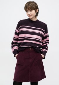 Sötétlila kötött pulóver rózsaszín vízszintes csíkokkal, bordó kordbársony szoknyával párosítva, melyen két első zseb található.