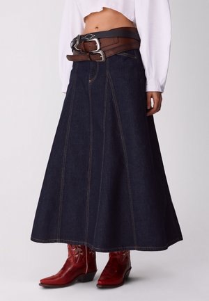 Falda acampanada de mezclilla oscura de talle alto combinada con dos cinturones de cuero y botas de vaquero rojas bordadas, usada con una blusa blanca corta.