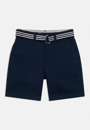 Tengerészkék hétköznapi rövidnadrágok oldalsó zsebekkel és fekete-fehér csíkos textil övvel, fém D-gyűrűs csattal.