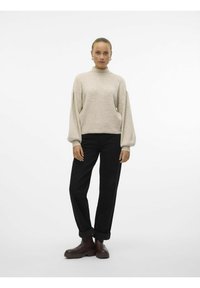 Pull en maille beige avec un col haut, des manches bouffantes et une coupe courte, associé à un pantalon noir à jambes larges et des bottines marron.