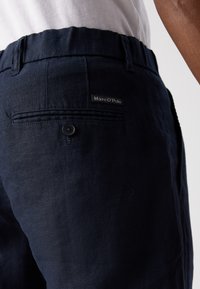 Pantaloni din in navy cu un buzunar la spate cu nasture, având un mic eticheta neagră cu textul "Marc O'Polo." Textură moale și croială lejeră.