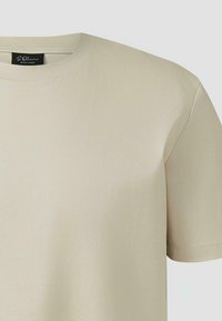 T-shirt beige à manches courtes et col rond avec coutures visibles et étiquette noire S.Oliver Black Label à l'intérieur du col.