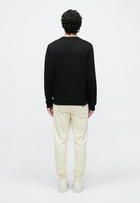 Fekete, hosszú ujjú pulóver bordázott mandzsettákkal, világos bézs melegítőnadrággal párosítva. Puha anyag, laza szabás. Fehér cipők láthatók.