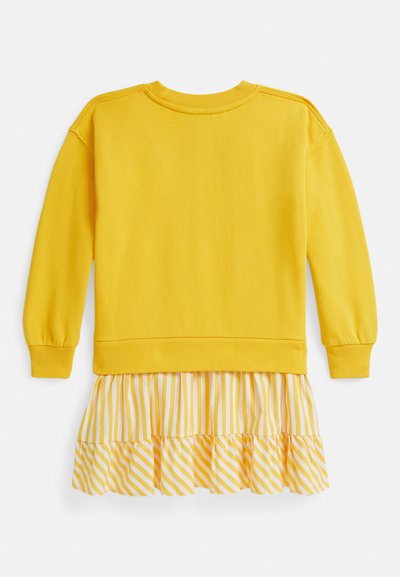 Geltonas džemperis su ribbintais rankogaliais ir apačia, derinamas su sluoksniuotu baltos ir geltonos spalvos dryžuotu sijonu, turinčiu dvi raukšlėtas pakopas.