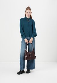 Tegenblauwe blouse met opgezette mouwen, gecombineerd met wijde blauwe jeans en een diep bordeaux leren schoudertas met een zilveren gesp.