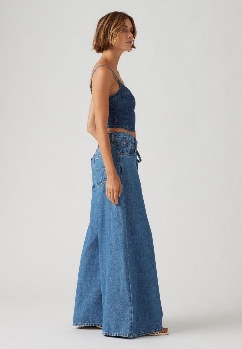 Top en denim court avec des fines bretelles et un jean large taille haute, tous deux en bleu moyen, avec un design de poche arrière en forme de cœur.