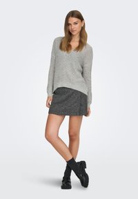 Pull en maille gris à col en V, associé à une jupe à carreaux foncés. Le mannequin porte des mocassins noirs et des chaussettes grises montant jusqu'au genou. Design simple et texturé.