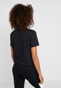 Černé zkrácené tričko s krátkým rukávem, vyrobené z bavlny, s jednoduchým designem a jemnou texturou, doplněné o černé legíny.