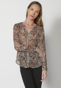 Blusa trasparente con maniche lunghe in tonalità terrose, decorata con un motivo a foglie, dotata di chiusura a bottoni e orlo arrotondato.