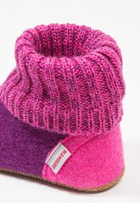 Różowy i fioletowy filcowy but z wełny z prążkowanym dzianinowym mankietem i znakiem firmowym, charakteryzujący się miękką teksturą i zaokrąglonym kształtem.