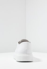 Scarpa bianca in pelle con una superficie liscia, forma arrotondata e una spessa suola in gomma bianca caratterizzata da scanalature orizzontali.