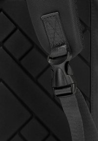 Cintura nera regolabile con una fibbia in plastica, tessuto testurizzato e uno sfondo decorato con un design a diamante.