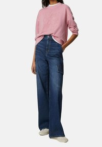 Sudadera rosa con el texto "New York City" y pantalones cargo de denim amplios y azules, con bolsillos y un ajuste relajado. Zapatillas neutras completan el look.