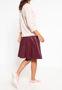 Lichtroze top met een textuurpatroon, bordeaux faux leren rok en lichtroze sneakers. De rok heeft een uitlopende stijl en naaddetails.