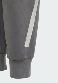 Grå sweatpants med en texturerad tygkonstruktion, ribbad mudd och ett vertikalt vitt accentband präglat med årtal.