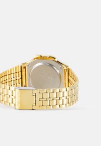 Montre en métal doré avec un bracelet à maillons texturé et un boîtier rectangulaire. Comprend un dos en argent et le nom de la marque gravé sur le fermoir.