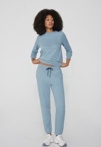 Jasnoniebieska bluza z długim rękawem i okrągłym dekoltem, w połączeniu z dopasowanymi spodniami dresowymi z elastycznym pasem i sznurkiem.