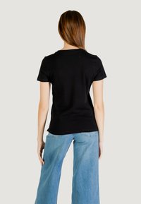 T-shirt nera a maniche corte con silhouette aderente, realizzata in cotone morbido, abbinata a jeans azzurri a gamba larga. Design semplice e pulito.