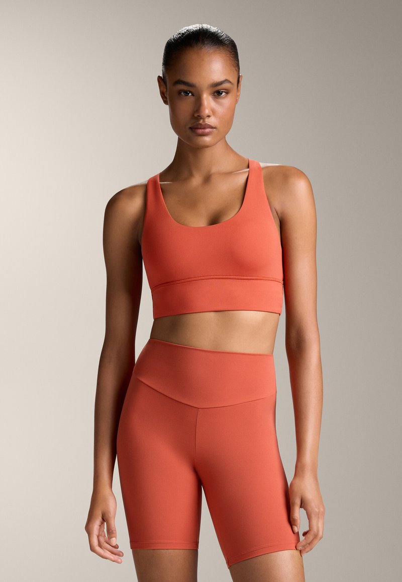 Narancssárga sport crop top, valamint a hozzá illő, magas derekú sort, rugalmas anyagból. A dizájn kivágott nyakkivágással és testhezálló siluettel rendelkezik.