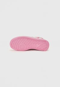 Semelle de sneaker en caoutchouc rose avec un motif de bande de roulement texturé et un élément de logo circulaire. La semelle présente de profondes rainures pour une meilleure adhérence.