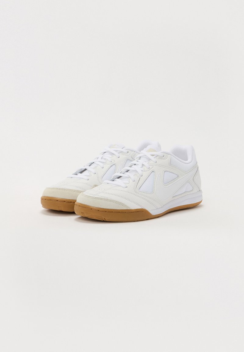 Zapatillas deportivas blancas con un upper sintético texturizado, paneles de malla y una suela de goma. Características de punta redondeada y cierre de cordones.