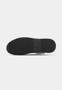 Brązowa i czarna podeszwa sneakerów z teksturowanym wzorem gumowym, składającym się z zazębiających się kształtów dla lepszej przyczepności. Płaska z zaokrąglonym noskiem.