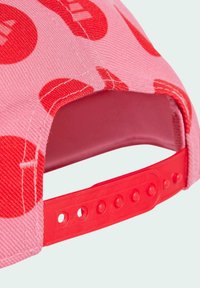 Cappello rosa con motivi circolari rossi, dotato di una fascia regolabile in plastica rossa e tessuto testurizzato. Anche l'interno è rosa.