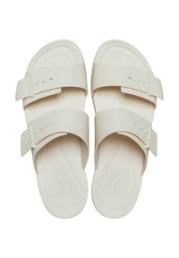 Light beige slide sandals made of smooth rubber with two adjustable straps featuring small holes for fit. Textured footbed for comfort.