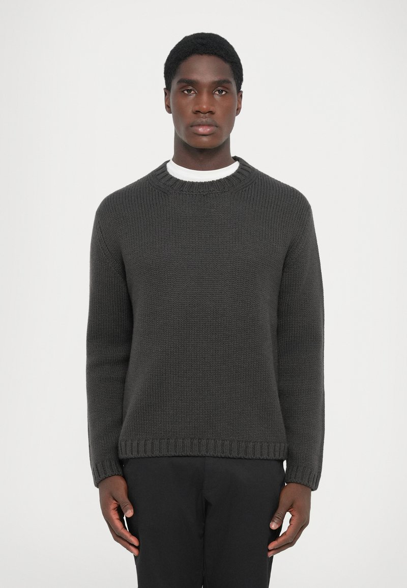 Dark gray knitted crew-neck sweater with ribbed cuffs and hem, featuring a textured pattern. Worn over a white shirt.