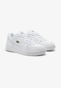 Sneakers bianchi in pelle con suola piatta, collo imbottito e design con lacci. Presentano un piccolo logo verde di lato e dettagli perforati.