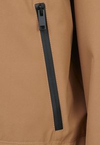 Tan jacket fabric with a black zippered pocket detail. Smooth texture and visible stitching along the edges.
