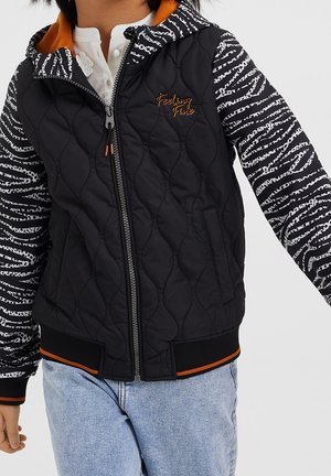 Sort quiltet jakke med lynlåslukning, orange hætteforing og stribede ærmer i sort og hvidt mønster. Har ribbede manchetter og kant.