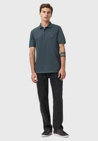 Mørkegrå polo shirt med korte ærmer, krave og subtilt logo-detalje; parret med sorte jeans og grå sneakers.