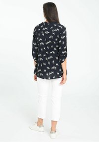 Blouse navy avec un motif animal subtil, manches 3/4 et encolure ronde. Associée à un pantalon blanc cropped et des baskets avec des accents argentés.