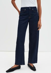 Jeans a gamba larga blu navy con vita alta, cuciture arancioni a contrasto, cinque tasche e chiusura con bottone. Tessuto denim liscio.