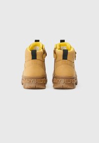 Botas de cuero marrón claro hasta el tobillo con una suela de goma texturizada, que presentan un forro interior amarillo, detalles en negro y "TOMMY HILFIGER" grabado en el talón.