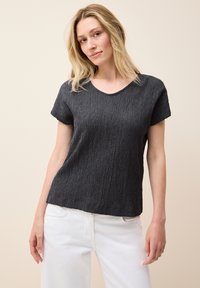 Sort tekstureret T-shirt med korte ærmer og dyb udskæring, sat sammen med lysfarvede jeans. Stoffet har et ribbet mønster.