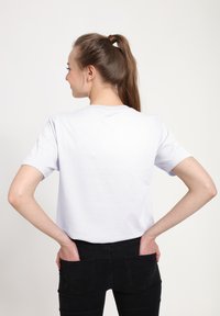 Biała bawełniana koszulka z krótkim rękawem, okrągłym dekoltem, minimalistycznym wzornictwem i lekko luźnym krojem, noszona z czarnymi dżinsami.