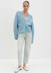 Cardigan lavorato a maglia di un blu chiaro con scollatura a V, texture a coste e bottoni sul davanti. Abbinato a jeans chiari a gamba dritta e scarpe bianche.