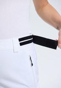 Pantaloni bianchi con un cinturino regolabile in Velcro nero. Presentano una tasca laterale con zip e una texture liscia. Design semplice e funzionale.